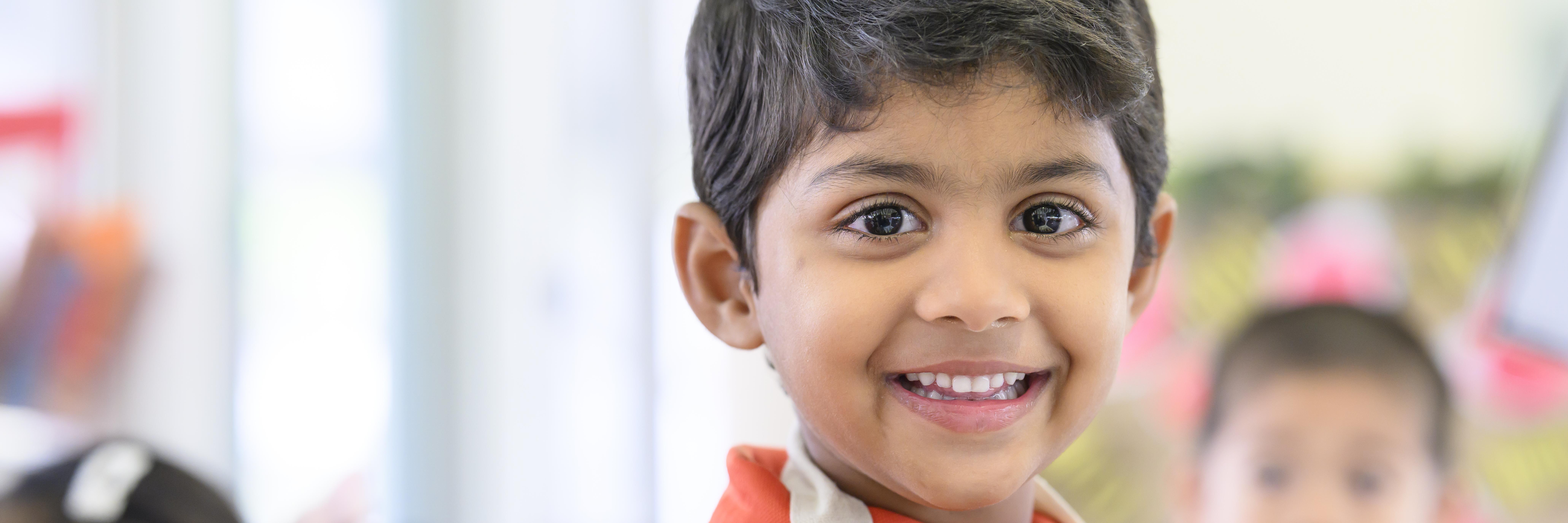 Little boy looking towards the camera with a big grin, close up of his face