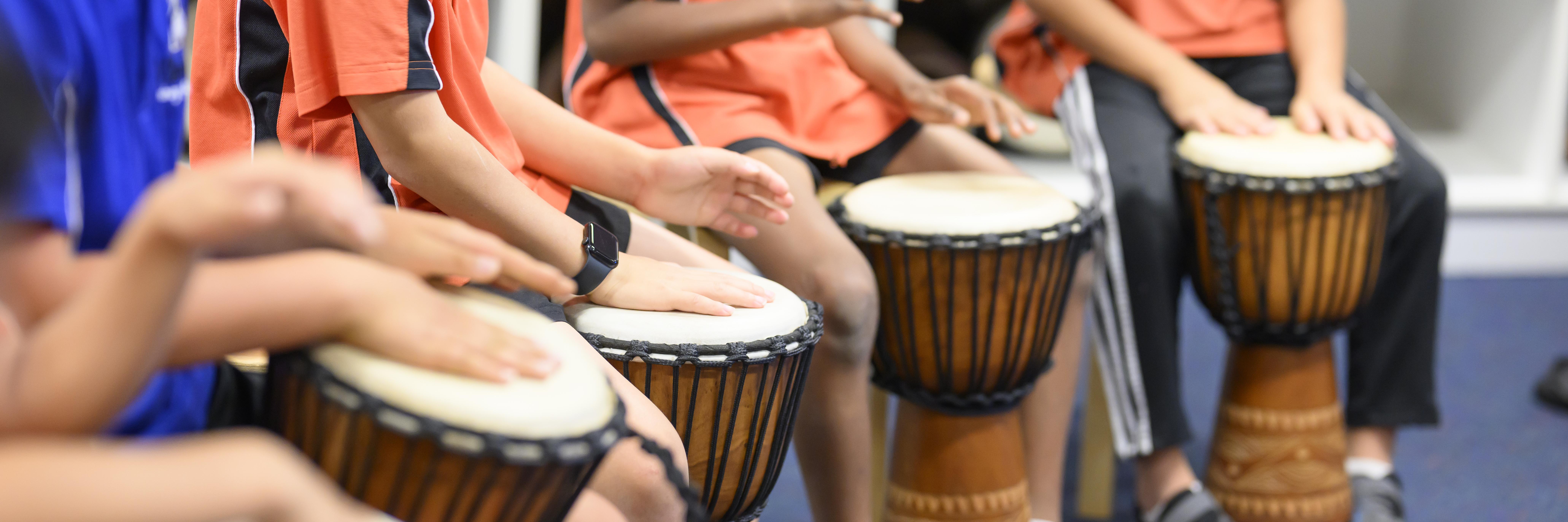four drums in center of image, boys in motion of banging the drums with their hands. drum in main focus is being hit by a boy with a smart watch on 